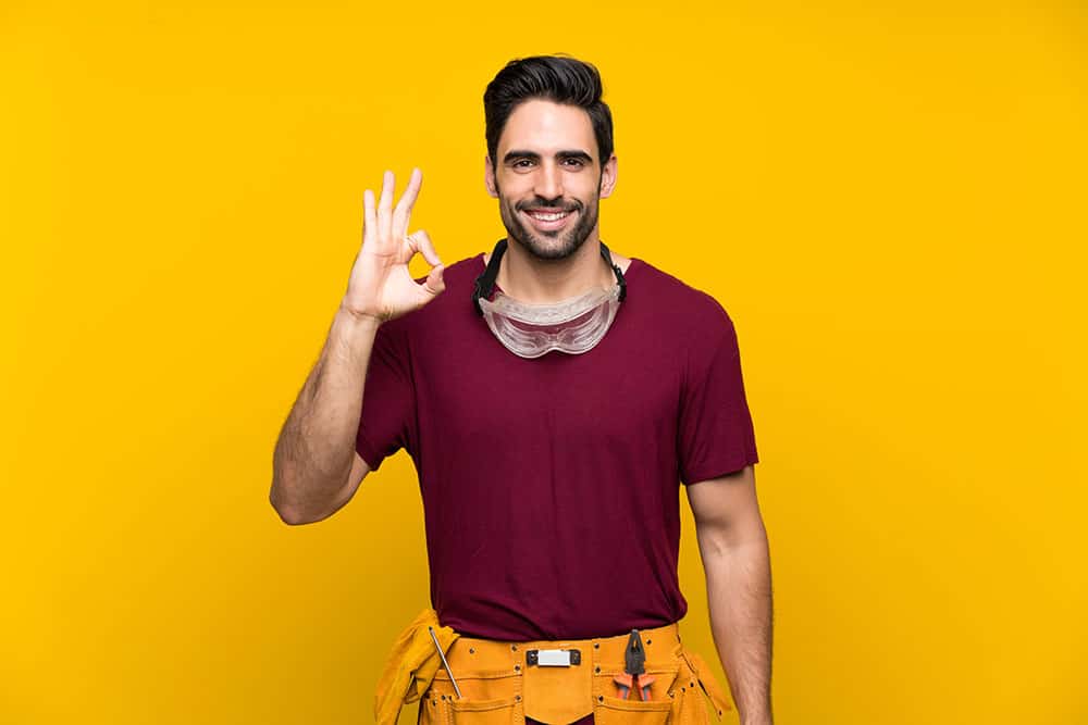 Handsome young craftsman over isolated yellow background showing ok sign with fingers